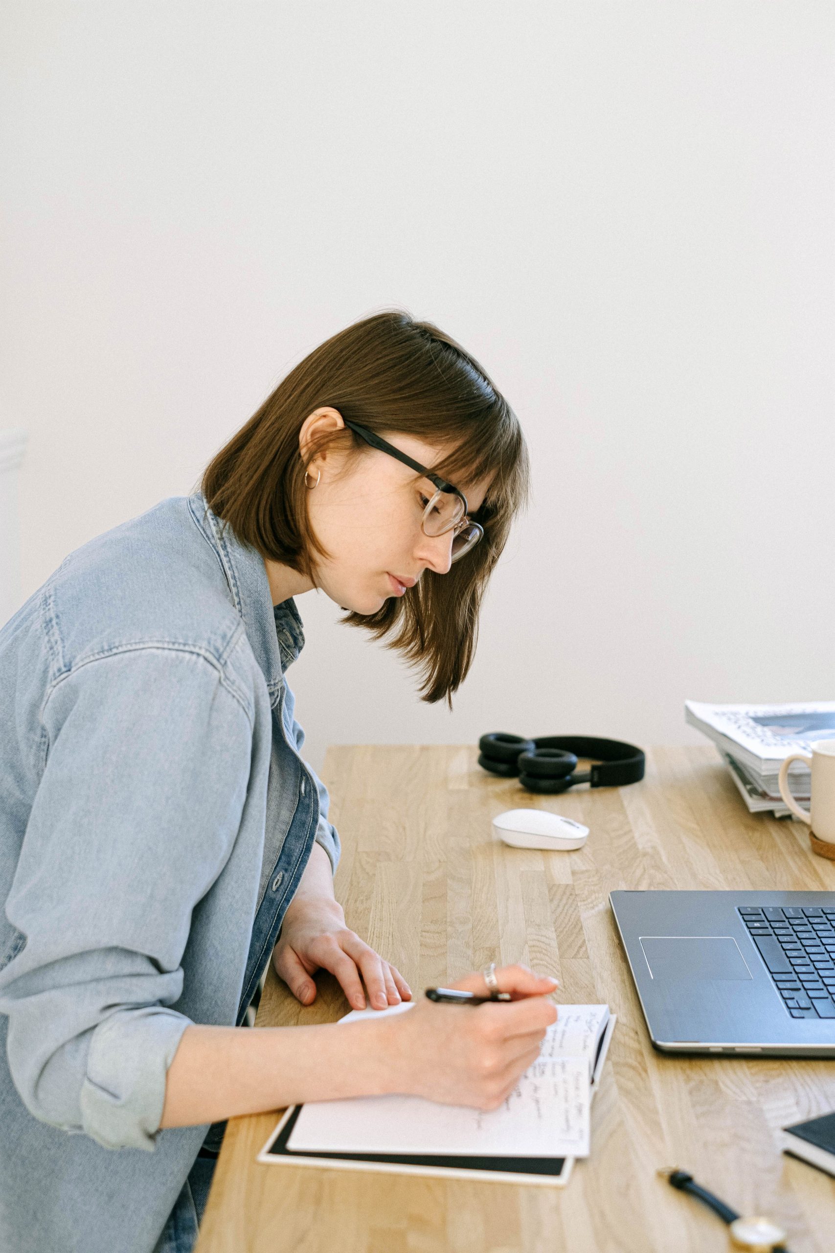Femme concentrée qui prend des notes dans un bureau cosy avec ordinateur portable, écriture de blog